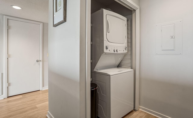 laundry room featuring electric panel, stacked washer and dryer, light hardwood / wood-style flooring, and a textured ceiling