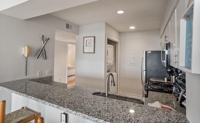 kitchen with kitchen peninsula, light stone countertops, stacked washer and clothes dryer, and sink