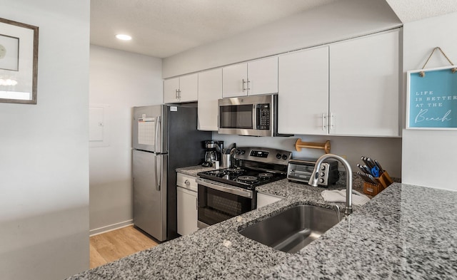 kitchen with light hardwood / wood-style flooring, stainless steel appliances, sink, light stone countertops, and white cabinets