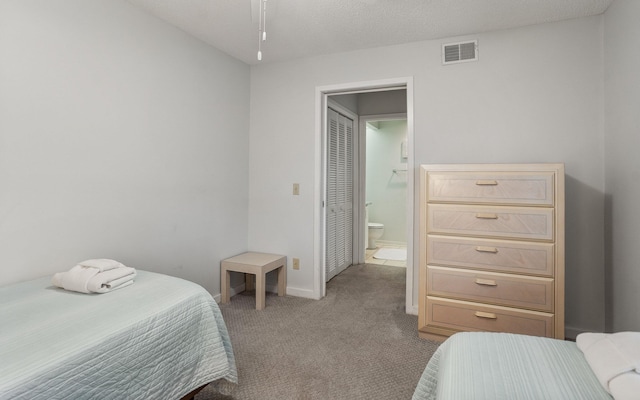 bedroom with ensuite bath, light carpet, and a textured ceiling