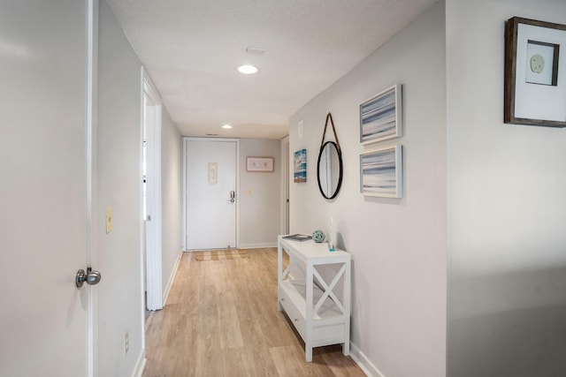 corridor with a textured ceiling and light hardwood / wood-style floors