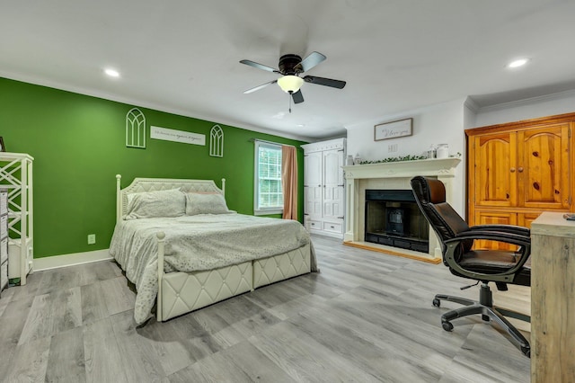 bedroom with a fireplace with raised hearth, baseboards, ornamental molding, recessed lighting, and light wood-style flooring