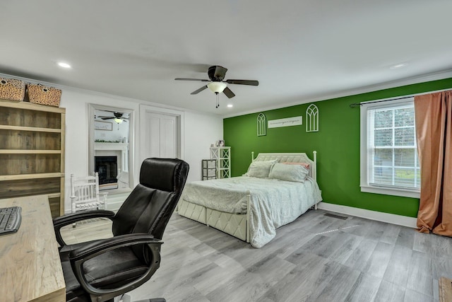 bedroom featuring a fireplace with raised hearth, wood finished floors, baseboards, and ornamental molding