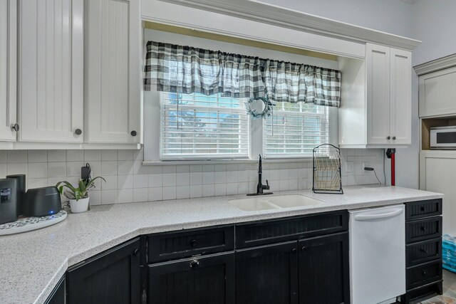 kitchen featuring a sink, backsplash, dark cabinetry, white dishwasher, and light countertops