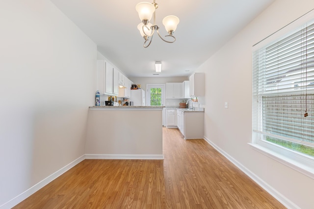 kitchen with light wood-type flooring, freestanding refrigerator, a chandelier, and light countertops