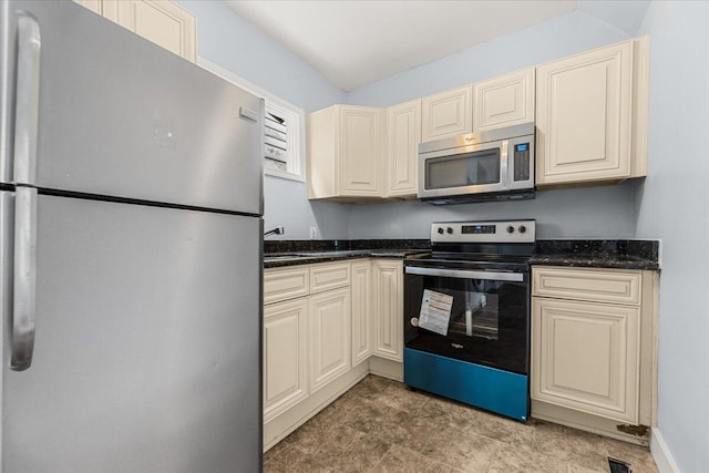 kitchen featuring appliances with stainless steel finishes, cream cabinets, dark stone countertops, and sink