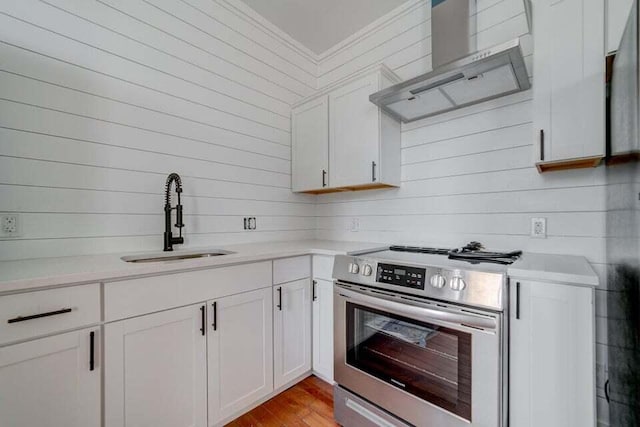 kitchen featuring wall chimney range hood, stainless steel electric stove, white cabinetry, and sink