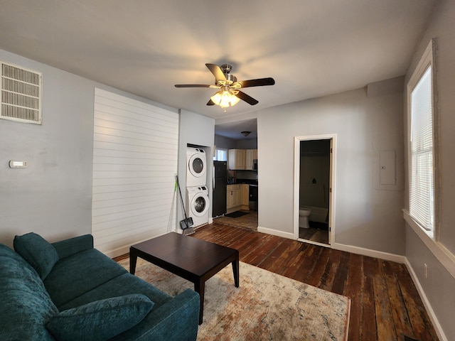 living room featuring ceiling fan, stacked washer / dryer, and dark hardwood / wood-style flooring