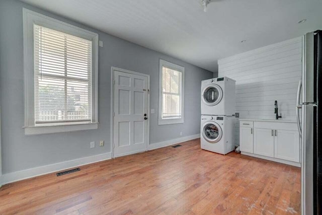 laundry area featuring cabinets, stacked washing maching and dryer, sink, and light wood-type flooring