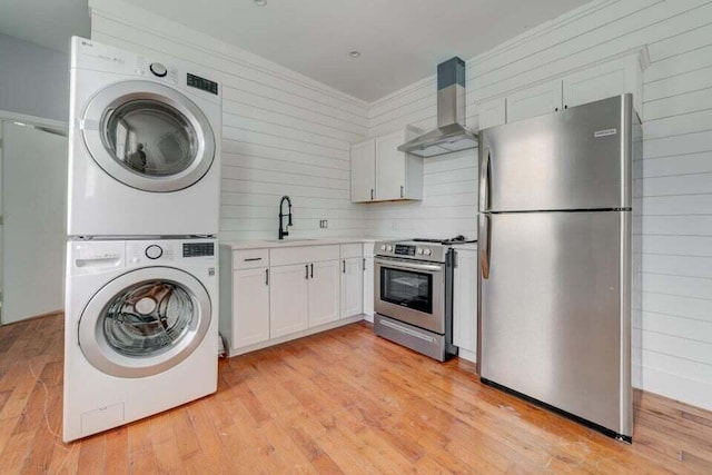 laundry area with sink, light hardwood / wood-style flooring, wood walls, and stacked washer and dryer