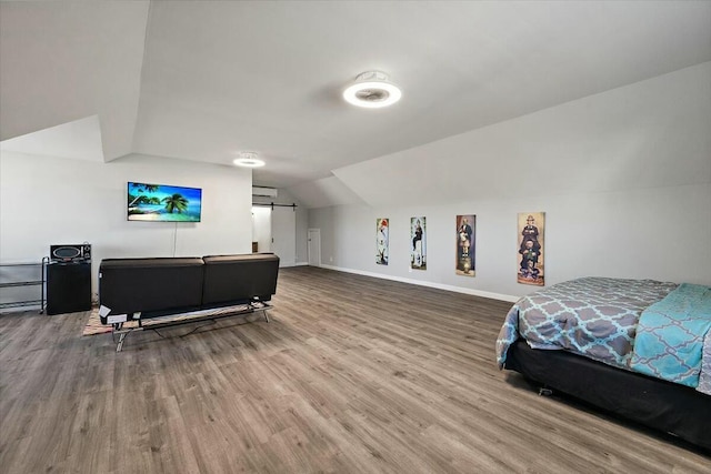 bedroom with baseboards, wood finished floors, a wall mounted AC, and vaulted ceiling