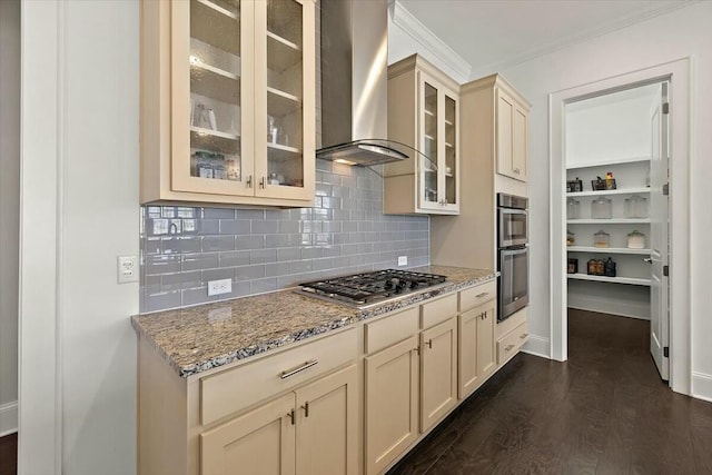 kitchen with light stone counters, cream cabinets, dark wood-style floors, stainless steel appliances, and wall chimney range hood