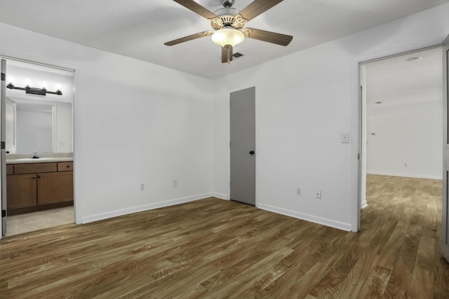 unfurnished bedroom featuring ceiling fan, ensuite bath, dark hardwood / wood-style floors, and sink