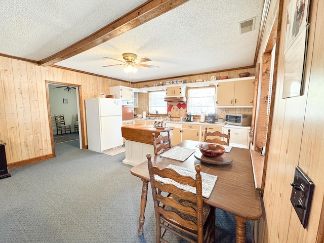 carpeted dining space with wood walls, beamed ceiling, a textured ceiling, and ceiling fan