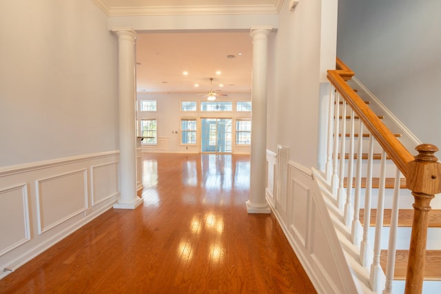 hallway with ornamental molding, a decorative wall, wood finished floors, and ornate columns