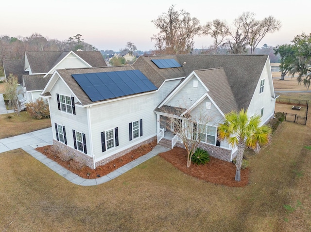 view of front of house with driveway, roof with shingles, fence, roof mounted solar panels, and a front yard