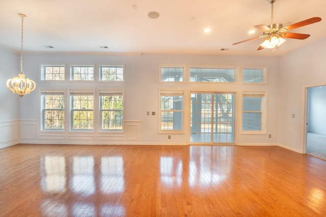 unfurnished living room featuring crown molding, ceiling fan with notable chandelier, a decorative wall, and hardwood / wood-style flooring