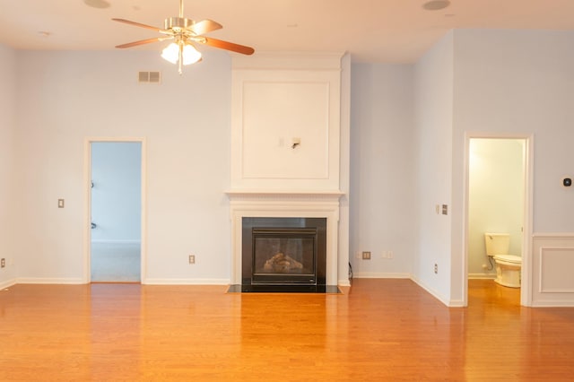 unfurnished living room featuring wood finished floors, a fireplace with flush hearth, baseboards, visible vents, and a ceiling fan