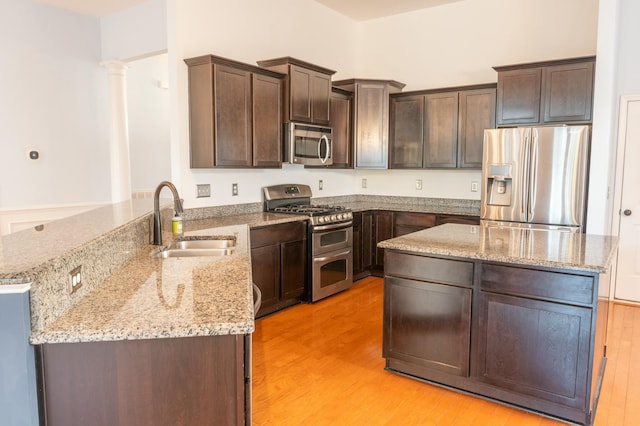 kitchen featuring light stone counters, stainless steel appliances, a sink, dark brown cabinets, and a peninsula