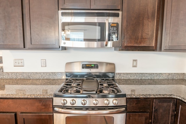 kitchen with stainless steel appliances, dark brown cabinets, and light stone countertops