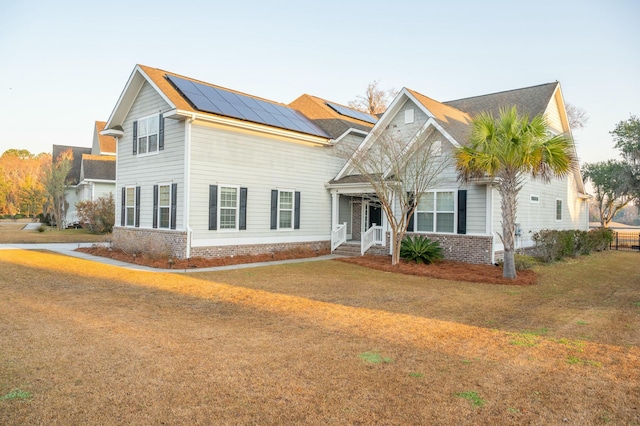 view of front of home with a front yard, metal roof, a standing seam roof, roof mounted solar panels, and brick siding