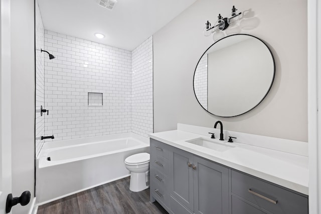 full bathroom with hardwood / wood-style flooring, tiled shower / bath combo, vanity, and toilet