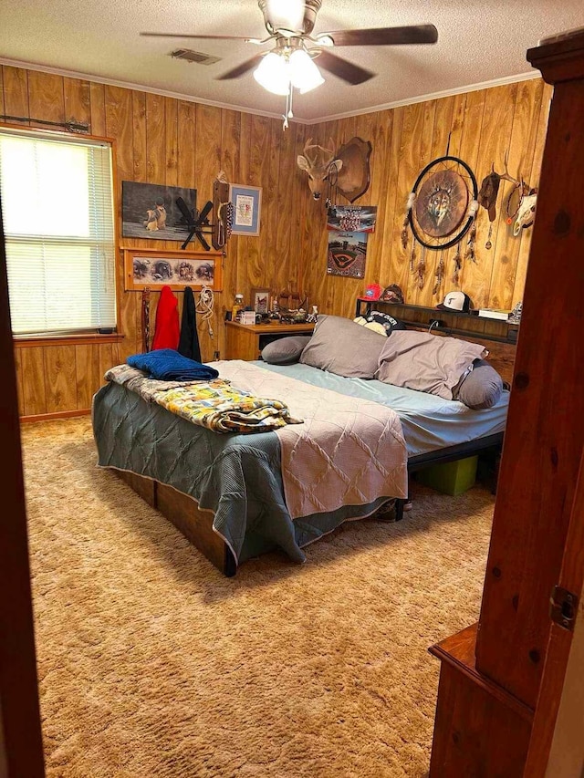 carpeted bedroom featuring visible vents, a ceiling fan, a textured ceiling, crown molding, and wood walls