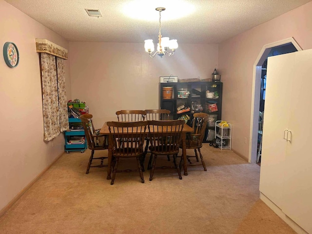 carpeted dining area with visible vents, arched walkways, an inviting chandelier, and a textured ceiling