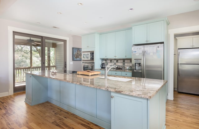 kitchen featuring light stone counters, stainless steel appliances, a spacious island, sink, and light hardwood / wood-style floors