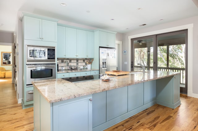 kitchen featuring light stone countertops, a large island, stainless steel appliances, and light wood-type flooring