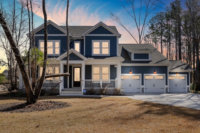 craftsman-style home featuring an attached garage, covered porch, concrete driveway, roof with shingles, and a front yard