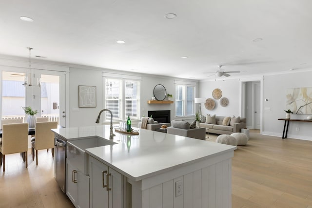 kitchen featuring ornamental molding, light wood-type flooring, a sink, and a center island with sink