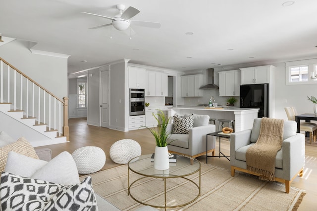 living area with ornamental molding, ceiling fan, stairway, and light wood finished floors