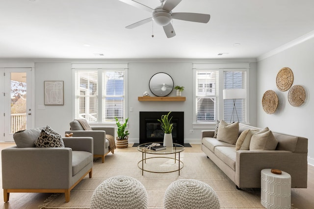 living room with a fireplace with flush hearth, a ceiling fan, baseboards, ornamental molding, and light wood finished floors