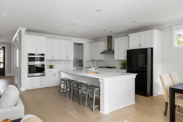 kitchen featuring a breakfast bar area, light countertops, wall chimney exhaust hood, light wood-type flooring, and black appliances