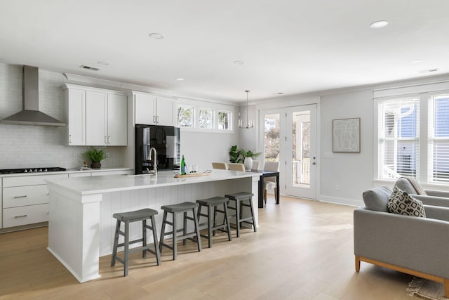 kitchen with refrigerator, a breakfast bar area, light wood finished floors, a kitchen island with sink, and wall chimney range hood