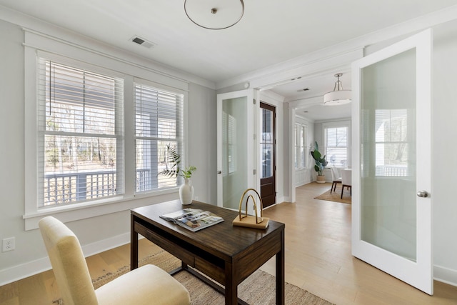 office space with baseboards, ornamental molding, visible vents, and light wood-style floors