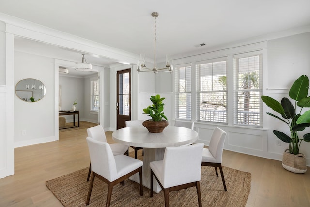 dining space featuring light wood-style floors, visible vents, a decorative wall, and ornamental molding