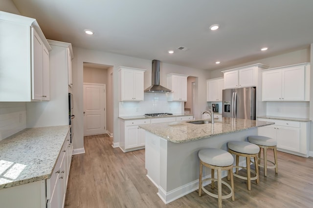 kitchen featuring white cabinets, wall chimney exhaust hood, a kitchen island with sink, and stainless steel appliances