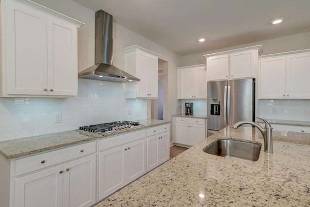 kitchen with wall chimney range hood, a sink, appliances with stainless steel finishes, and white cabinets