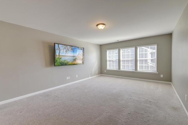 spare room featuring light colored carpet and baseboards