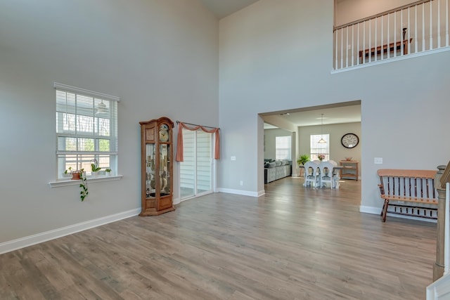 unfurnished living room with light wood-type flooring, a towering ceiling, and baseboards