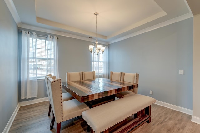 dining room with light wood-type flooring, a tray ceiling, a notable chandelier, and baseboards