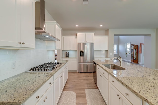 kitchen with light stone counters, stainless steel appliances, white cabinetry, a sink, and wall chimney exhaust hood