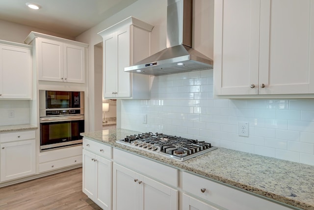 kitchen featuring stainless steel appliances, white cabinetry, light wood-style floors, wall chimney exhaust hood, and tasteful backsplash