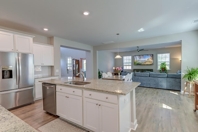 kitchen with a sink, white cabinetry, open floor plan, appliances with stainless steel finishes, and an island with sink