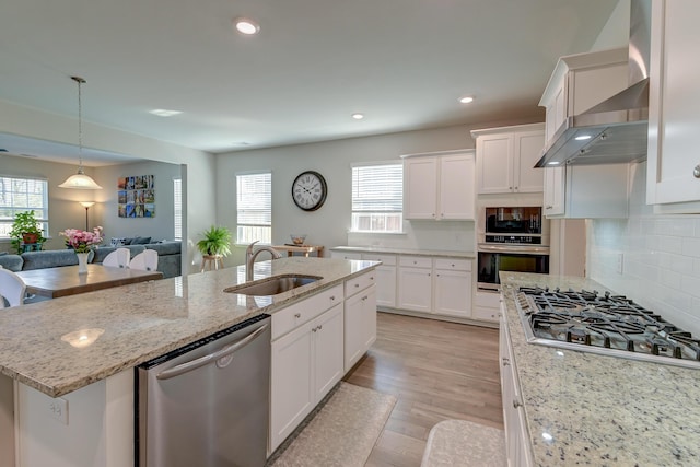 kitchen with stainless steel appliances, a sink, white cabinets, wall chimney exhaust hood, and a center island with sink