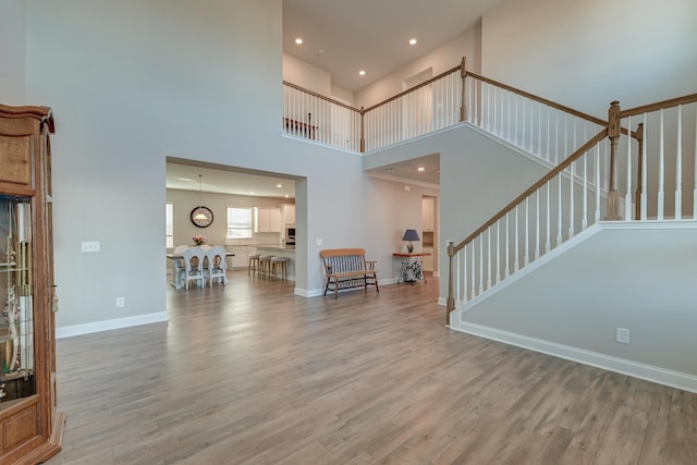 interior space with stairs, light wood finished floors, a towering ceiling, and baseboards