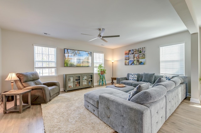 living area with light wood-style flooring, a ceiling fan, visible vents, and a healthy amount of sunlight