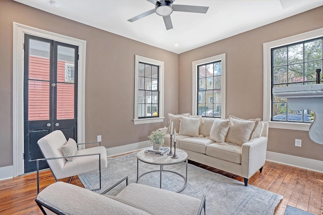 living area featuring baseboards, wood-type flooring, and a ceiling fan